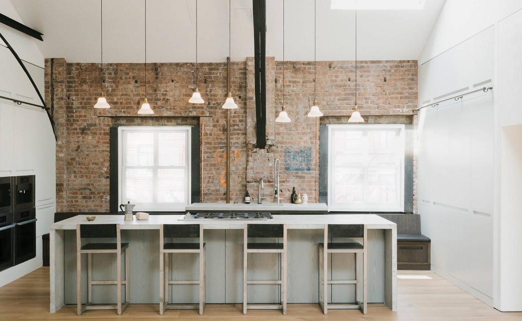 طراحی داخلی آشپزخانه مدرن با دیوارهای آجری که از چندین آویز کوتاه و بلند برای به وجود آوردن ریتم در آن استفاده شده است